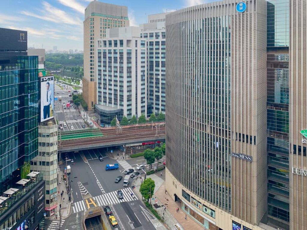 A high-angle view of the bustling streets of Chuo Tokyo, featuring modern skyscrapers, railway tracks, and busy intersections. The area showcases a blend of contemporary architecture and urban infrastructure, capturing the essence of Tokyo’s commercial hub.