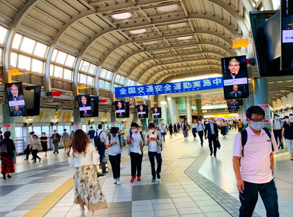 Inside a busy Tokyo Shinagawa train station, commuters walk under a modern arched roof with digital signage and banners, showcasing the city's efficient public transportation system.