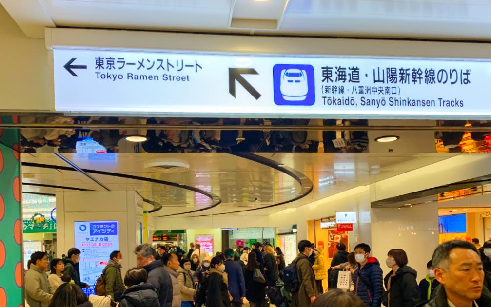 Entrance to Tokyo Ramen Street inside Tokyo Station, showing a directional sign and a bustling crowd of visitors near the ramen shops.