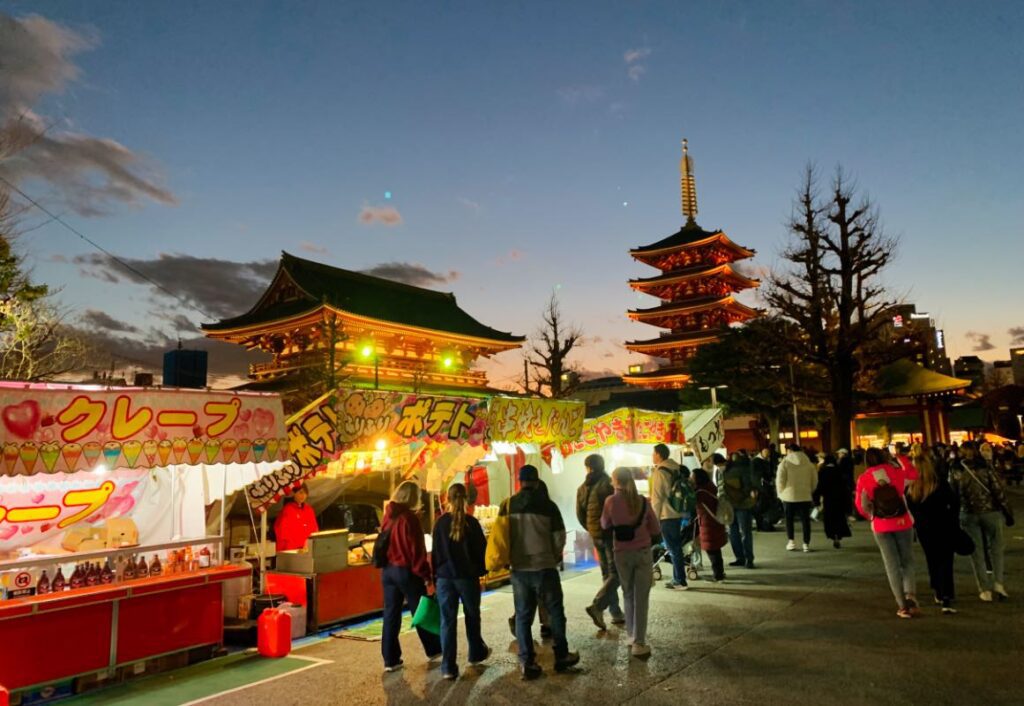 Night view of Senso-ji Temple in Asakusa during a lively festival, with food stalls and visitors enjoying the illuminated pagoda, highlighting Tokyo's cultural charm.