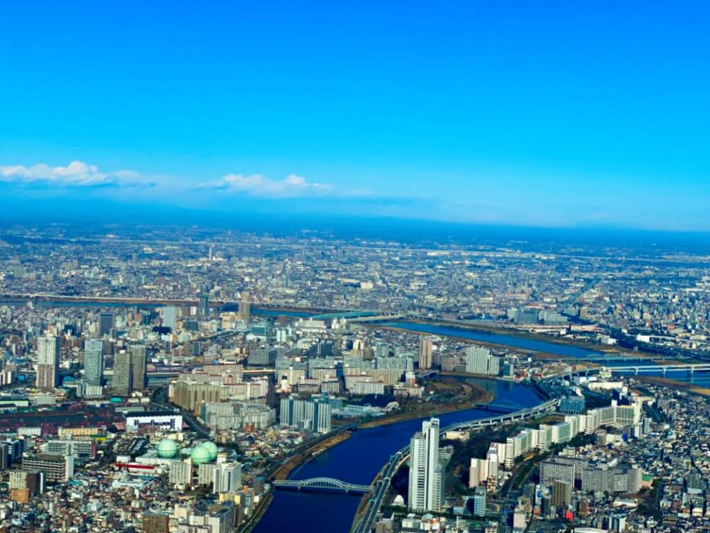 A panoramic view of Tokyo from Tokyo Skytree, showcasing the sprawling cityscape, rivers, and clear blue skies.