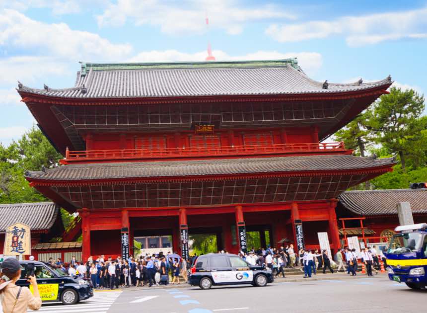 The historic Sangedatsumon Gate at Zojoji Temple in Tokyo, Japan, a grand red wooden structure with intricate architecture, surrounded by visitors and urban activity